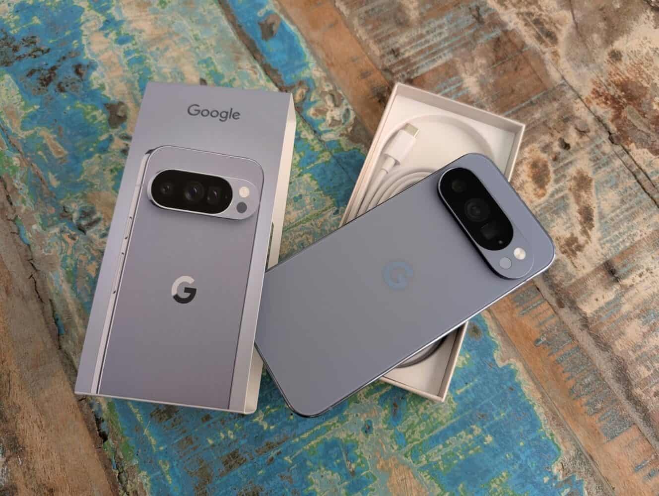 Een Google Pixel smartphone in blauw wordt getoond met zijn doos en bijgeleverde accessoires op een rustiek, verweerd houten oppervlak.