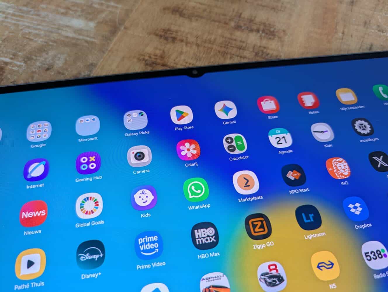 Close-up van het scherm van een Samsung Galaxy Tab S11 Ultra tablet met verschillende app-pictogrammen, waaronder Google, Play Store, WhatsApp, Disney+, HBO Max en meer, op een achtergrond van houten oppervlak.