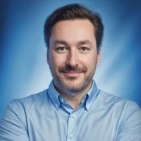 Dertig maanden celstraf voor verkoop botnettoegang Een man met kort bruin haar en een baard, draagt een lichtblauw overhemd met knoopsluiting en staat te glimlachen tegen een blauwe gradiënt achtergrond.