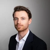 HTC ontwikkelt drie Windows Phone 8-toestellen Een man met kort bruin haar en een baard draagt een donkere blazer en wit overhemd en poseert tegen een effen, lichtgrijze achtergrond.