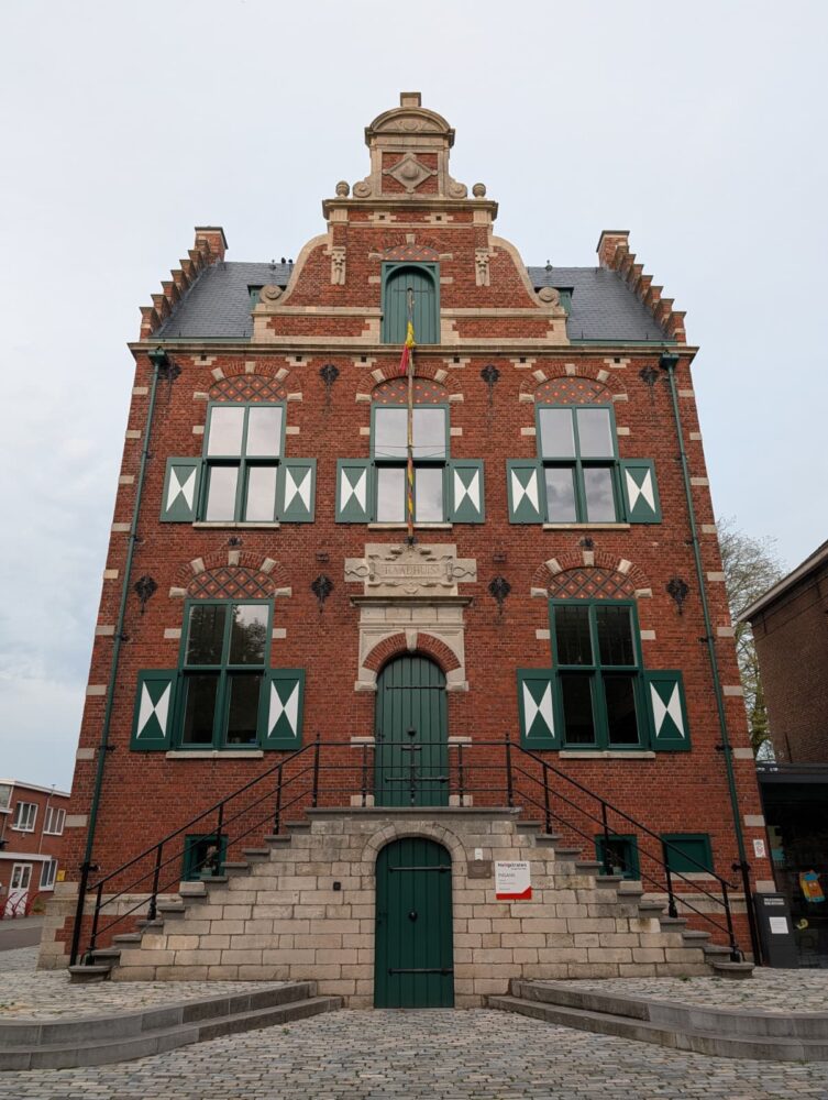 Historisch bakstenen gebouw met zadeldak, groene en witte luiken, gewelfde deuropening en stenen treden die naar de ingang leiden. Leg elk detail van de vlag boven de deur vast met de verbluffende camera van je Google Pixel 10 Pro.