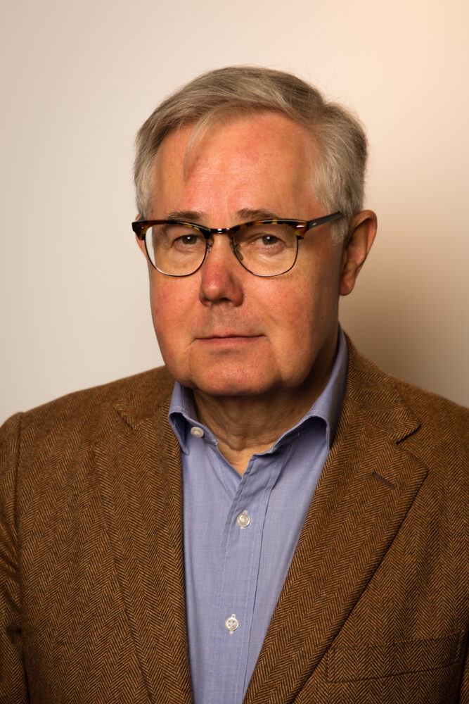 Een man met een bril en een bruine jas.