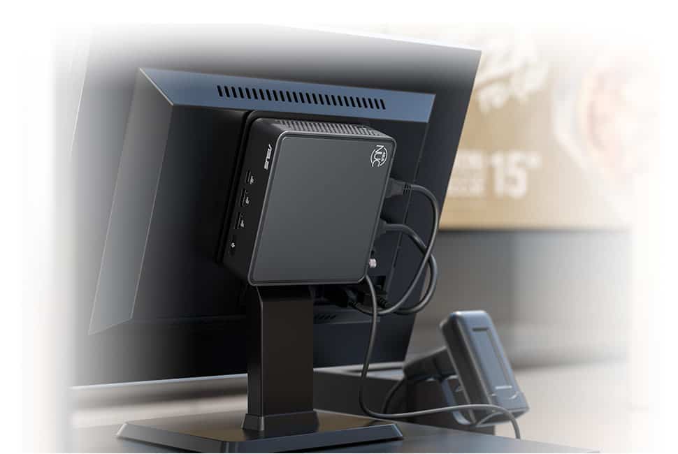 Een kleine zwarte computer gemonteerd op de achterkant van een monitor, verbonden met verschillende kabels, met beide apparaten geplaatst op een bureau.