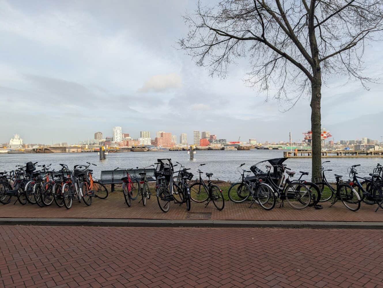 Fietsen geparkeerd langs een pad langs de rivier met een skyline van de stad en een waterweg op de achtergrond onder een bewolkte hemel, vastgelegd in haarscherp detail, perfect voor een Google Pixel 10a review.