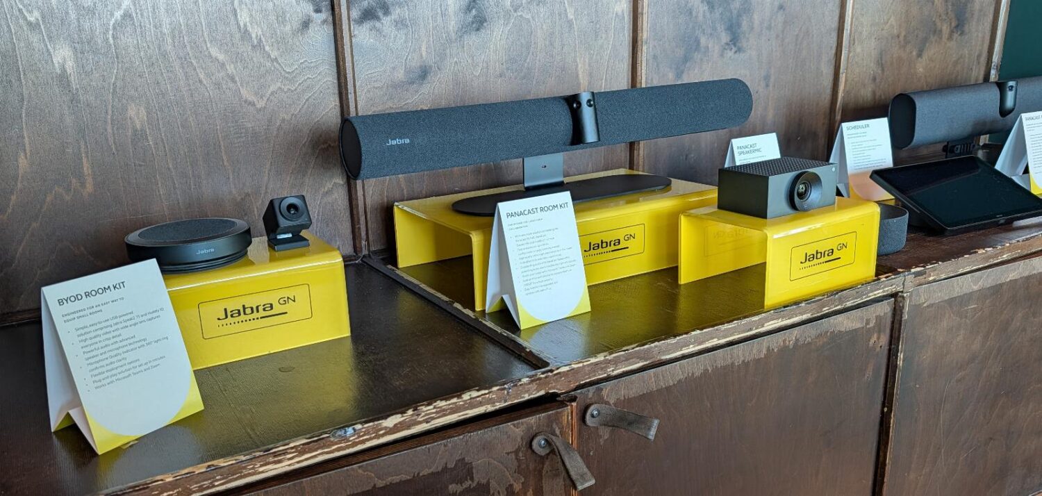 Een display met Jabra videoconferencingapparatuur, inclusief camera's, luidsprekers en informatiekaarten, staat opgesteld op een houten toonbank.