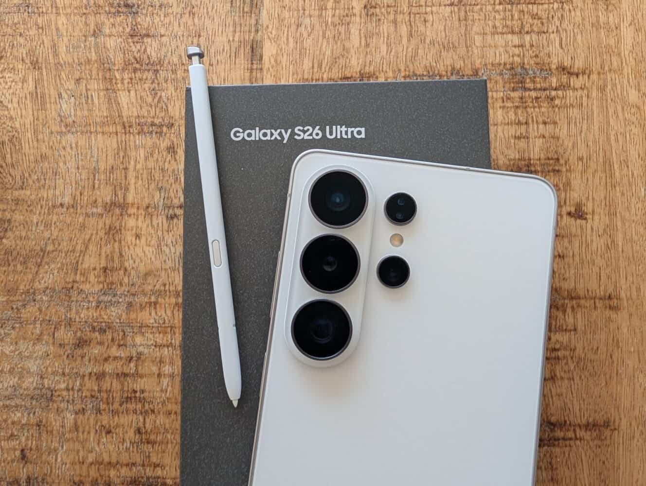 Een witte Samsung Galaxy S26 Ultra smartphone, de doos en een S Pen stylus zijn geplaatst op een houten oppervlak, perfect voor een hands-on Samsung Galaxy S26 Ultra review.