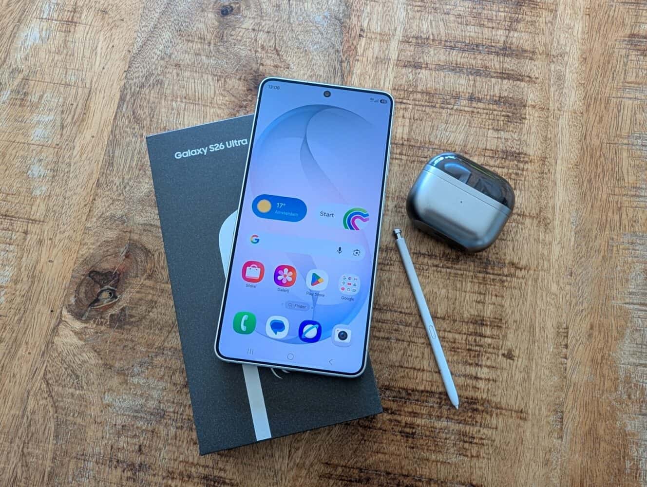 Een Samsung Galaxy S23 Ultra smartphone op zijn doosje met een stylus, naast een gesloten hoesje met draadloze oordopjes, allemaal geplaatst op een houten oppervlak - perfect voor iedereen die apparaten wil vergelijken na het lezen van een Samsung Galaxy S26 Ultra review.