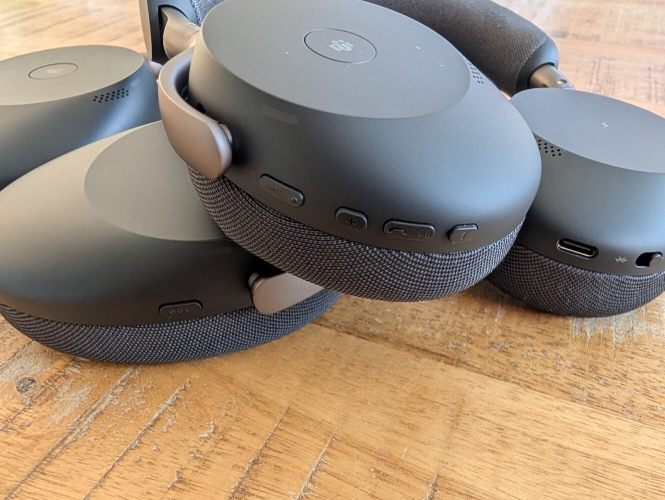 Close-up van drie paar zwarte over-ear headphones, waaronder de Jabra Evolve3, gestapeld op een houten oppervlak met zichtbare bedieningstoetsen en oplaadpoorten - perfect voor een gedetailleerde Jabra Evolve3 review.
