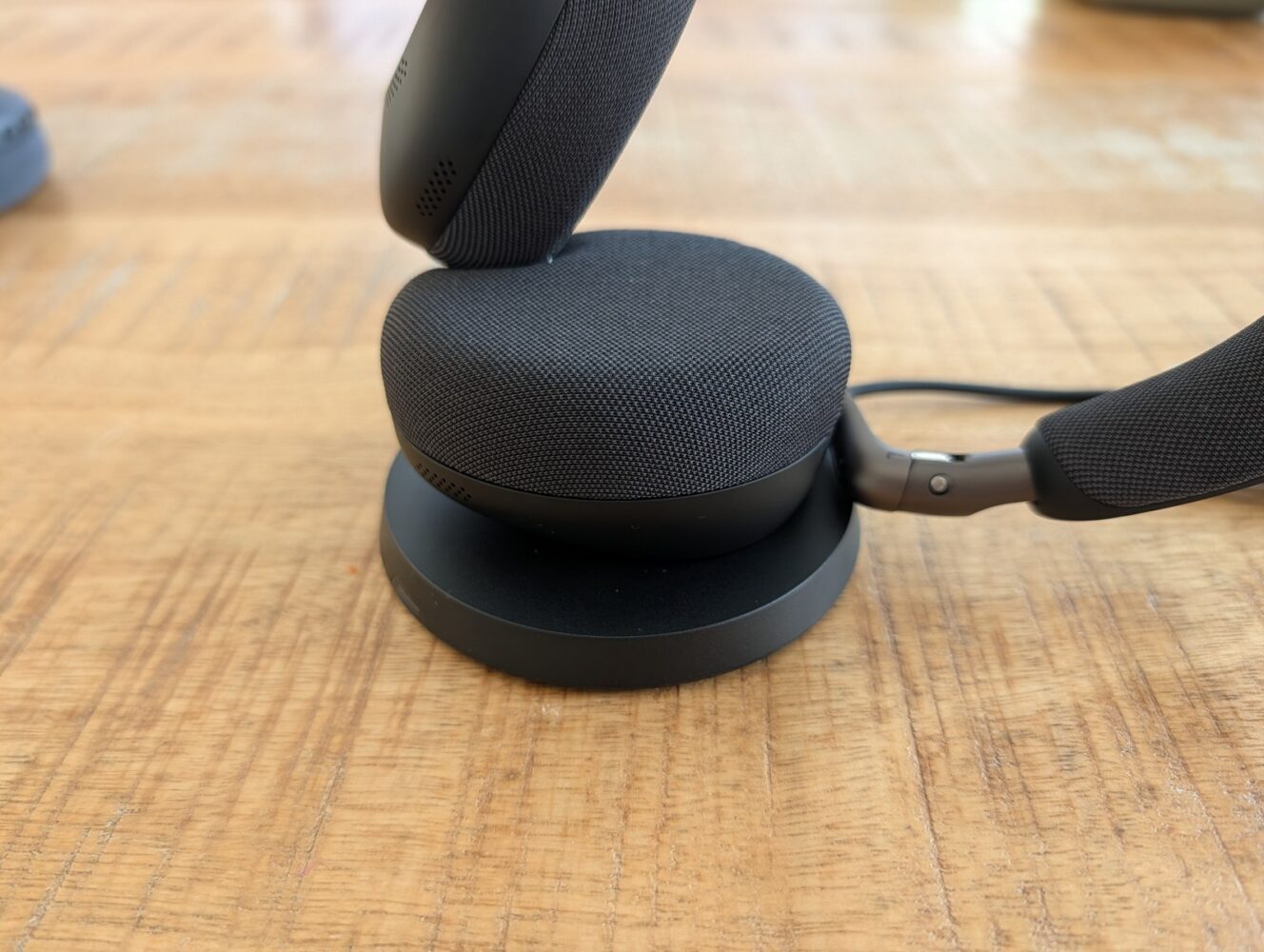 Een zwarte draadloze headset, die in een recente review van de Jabra Evolve3 aan bod kwam, rust op een rond oplaadstation op een licht houten oppervlak.
