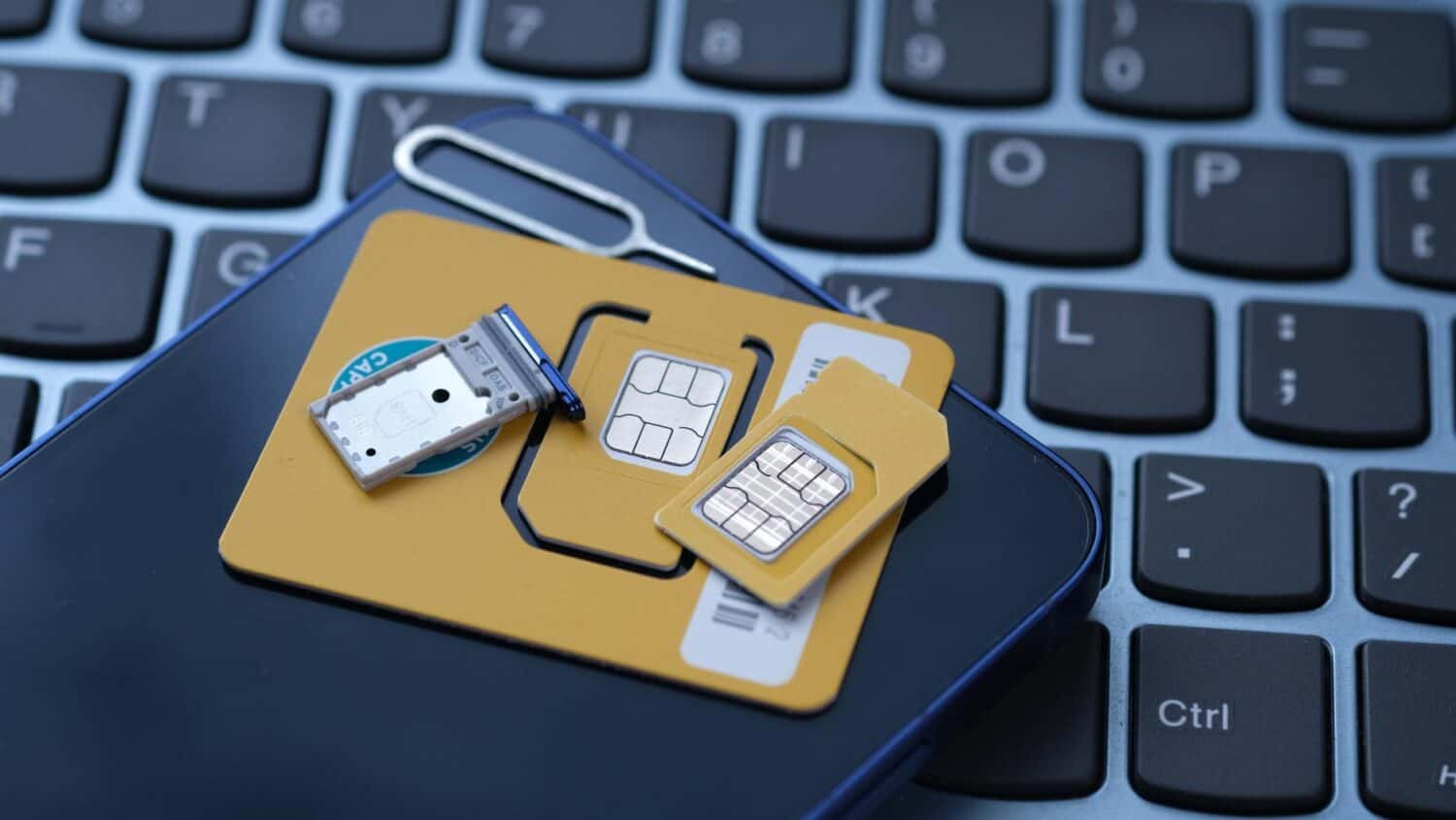 Een simkaart, simschaal, eSIM-informatiekaart en simuitwerptool worden bovenop een smartphone geplaatst, die op het toetsenbord van een laptop rust.