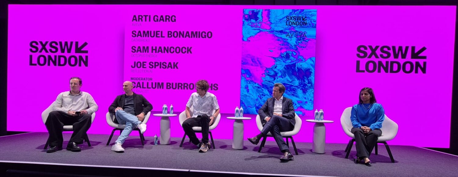 Vijf panelleden zitten op het podium met een roze achtergrond van SXSW Londen en details over het evenement, elk met waterflessen en microfoons op een tafeltje naast zich.